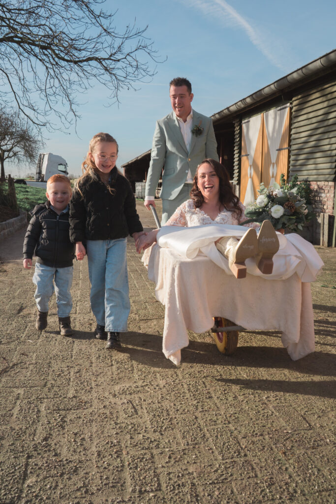Trouwreportage Genaenhof Swalmen bruidspaar in de kruiwagen met kinderen voor spontane fotoshoot